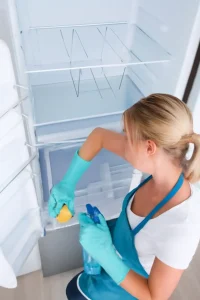 Woman cleaning fridge with gloves and spray bottle